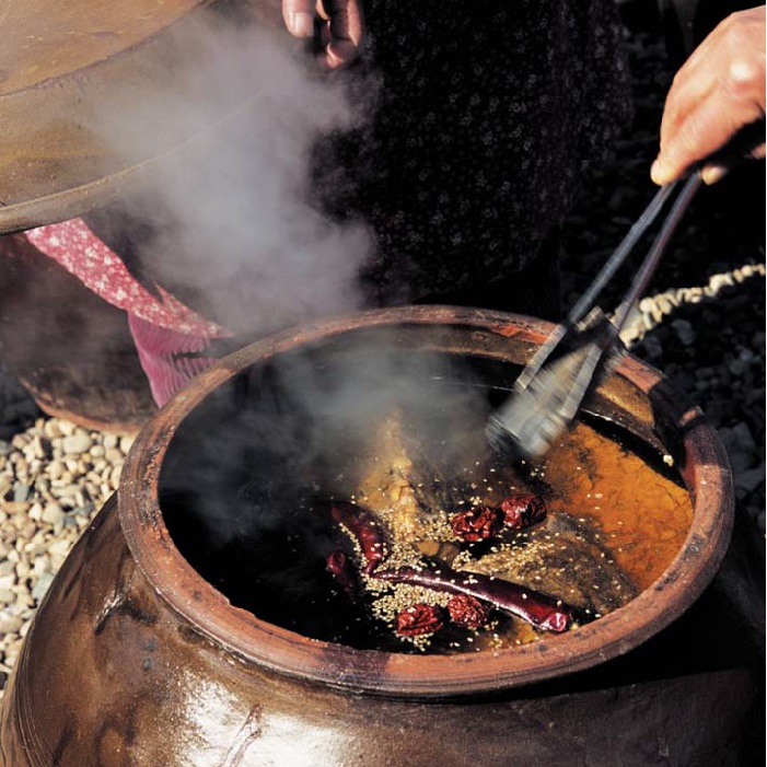 Soy sauce being prepared in a traditional urn is purified with hot charcoal. 