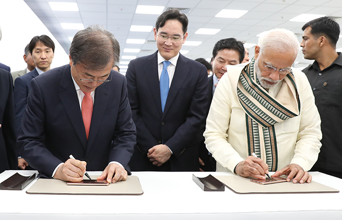 President Moon Jae-in (left) and Prime Minister Narendra Modi sign the backs of the first two phones made at the new Samsung factory in India, during their visit to the new facility on July 9. (Yonhap News)