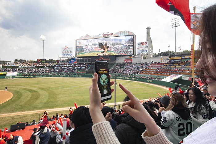 An SK Telecom model on March 23 uses a smartphone app to make an augmented reality wyvern fly higher on the opening day of the 2019 Korea Baseball Organization season at Incheon’s SK Happy Dream Park.