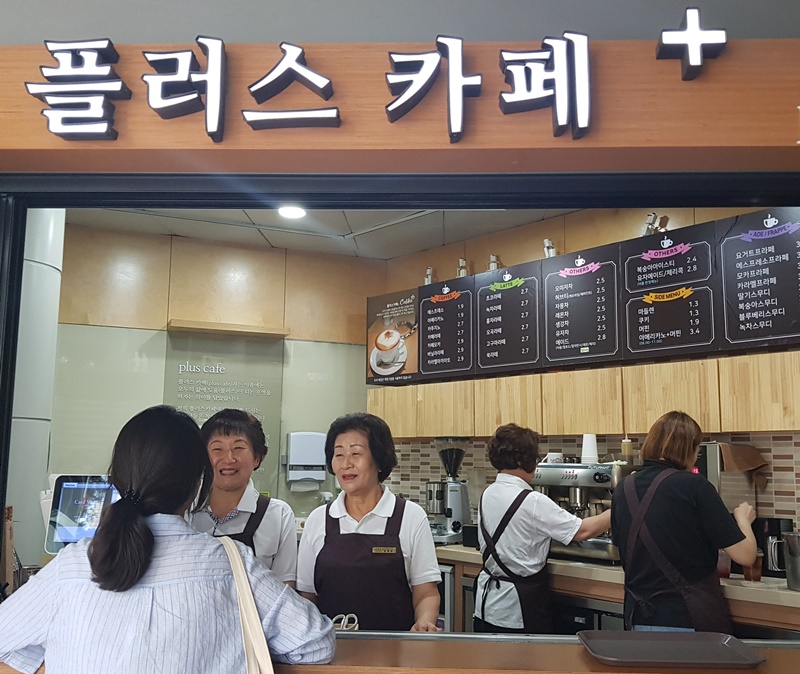 Kang Hwa-ja, 64, (left behind the counter) and Kim Myeong-suk, 74, (next to Kang) work as baristas at Plus Café in the building of Jongno-gu Office in downtown Seoul. (Kang Gahui)