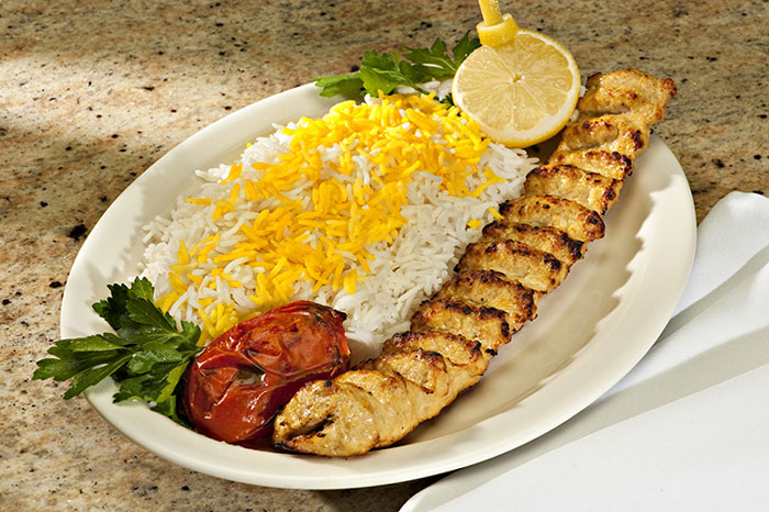An Iranian dish features a chicken kebab marinated in lemon juice and served with saffron, onions, grilled tomatoes and pickles.