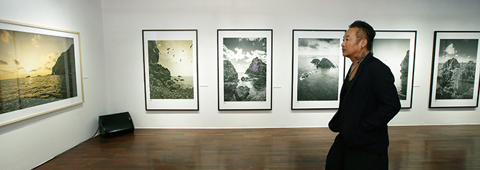Photographer Kim Jung-man admires his own works, on display in a photo exhibition at the Sejong Center for the Performing Arts on July 28. (photo: Jeon Han)