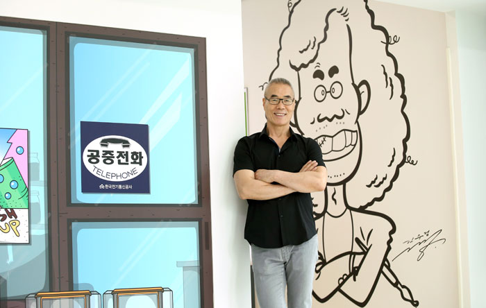 Kim Soo-jung, creator of 'Dooly, the Little Dinosaur,' poses for a photo in front of a larger-than-life caricature of himself at the Dooly Museum.