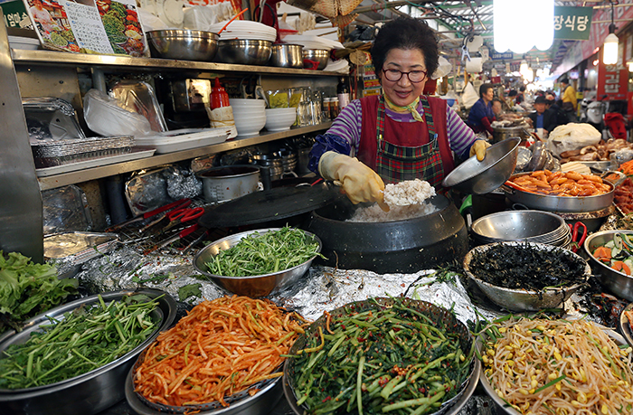Seo Geum-yeon prepares a bowl of <i>bibimbap</i>, mixed rice with various ingredients, as she scoops rice from an iron pot into a large bowl on April 10. She has been selling <i>bibimbap</i> for almost 20 years in the food alleys of Gwangjang Market in Jongno-gu District in central Seoul. (photo: Jeon Han)