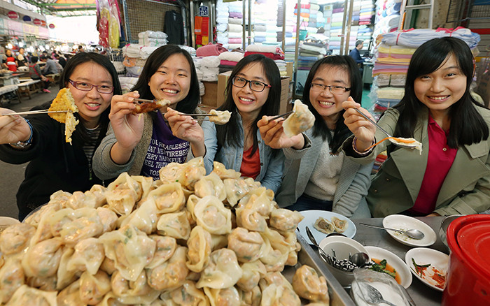 Lee Yee Jin and her friends, visiting the Gwangjang Market from Malaysia, pose for a photo holding up their steamed dumplings and <i>bindaetteok</i>. (photo: Jeon Han)