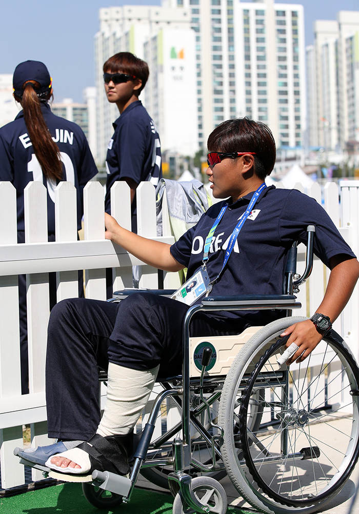 Korean female cricket player Kim Bokyung watches her colleagues warm up before the match against Hong Kong on September 22. Kim suffered an ankle injury the day before the match, but cheered for her teammates while wheel chair-bound, despite the hot weather.