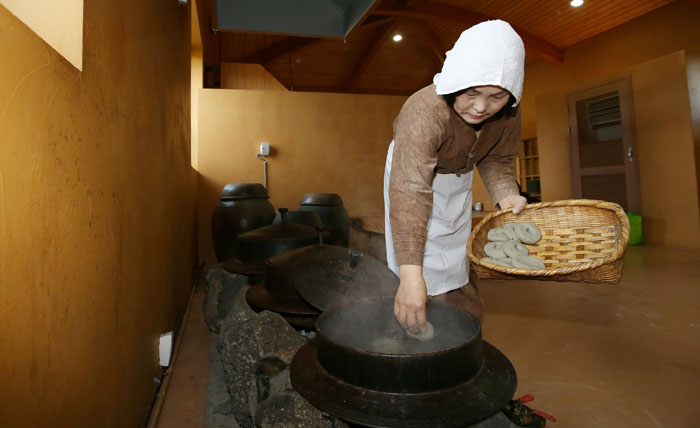 Kang Kyoung-soon, a master brewer of <i>omegisul</i>, places some <i>omegitteok</i>, traditional cakes made from millet into the boiling water. This is part of brewing <i>omegisul</i>, a traditional grain-based alcoholic beverage from Jeju Island.
