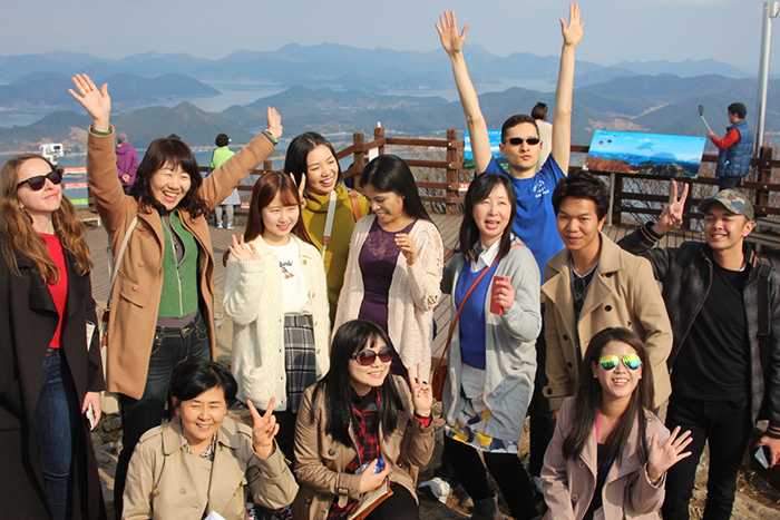 Tourists on the K-Travel Bus stop at the Mireuksan Moutain Observatory in Tongyeong, Gyeongsangnam-do Province. They take a picture with the islands of the Hallyeosudo in the background.