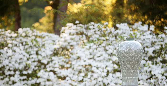 Against a backdrop of flowers, a replica Goryeo celadon vase shines its brilliant blue-green colors in the front garden of the Gangjin Celadon Museum.