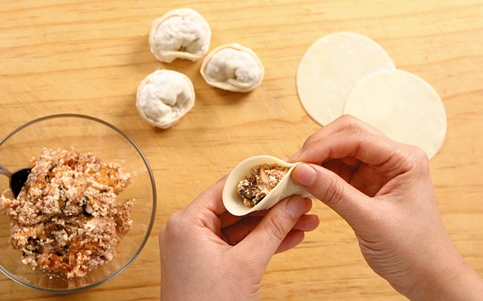 Put the filling in the center of the dumpling skin and fold it over to make round-shaped dumplings, twisting both ends together.