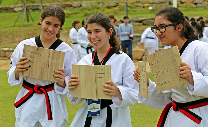 One taekwondo adherent (top) learns the basic taekwondo techniques. Three young trainees (bottom) smile as they hold pine boards to be smashed in half, boards on which they have written their weak points that they want to break. 