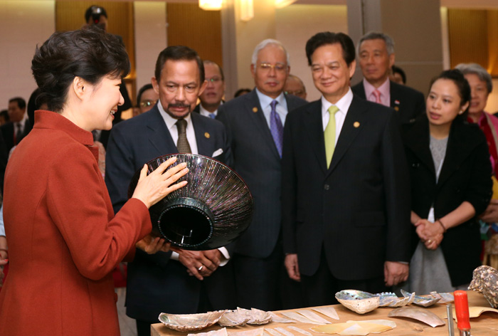 President Park Geun-hye (left) explains to leaders of the 10 ASEAN countries some of the traditional artistry on display, holding a work of lacquerware inlaid with mother-of-pearl. The heads of state were there to attend a welcome dinner at the BEXCO convention center in Busan on December 11. 