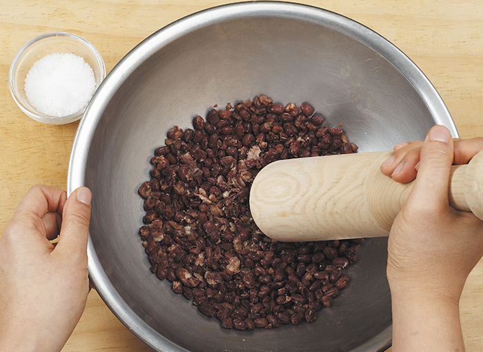 Heat the steamed red beans to remove any water and add salt when warm. Mash the red beans into half their size. Add salt to the red beans to make the taste deeper rather than sugary.