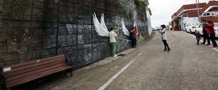 Visitors take a picture against a wall painting of feathers in the Dongpirang Village. 