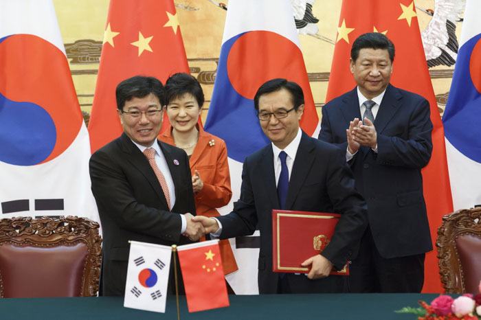 Trade ministers from Korea and China sign the Korea-China FTA, with leaders from Korea and China standing by.