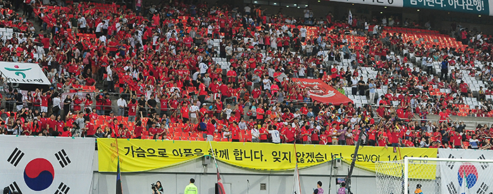 The Korean national soccer team fan club wears red shirts to cheer on its heroes while displaying a large yellow banner in mourning of the people who lost their lives in the tragic Sewol ferry sinking, at the Korea-Tunisia friendly on May 29. Prior to the match, there were 16 minutes of silence in honor of the 16 people still missing from the ferry disaster. (photo: Jeon So-hyang, Ministry of Culture, Sports and Tourism)