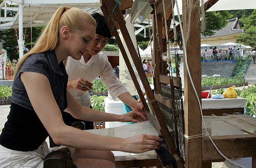 A foreign tourist participates in a hands-on ramie fabric-weaving activity offered at the Hansan Mosi Cultural Festival (photo courtesy of Seocheon County).