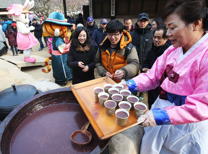 A staffer at the Korean Folk Village in Yongin City, Gyeoggi-do Province, offers <i>patjuk</i>, or rice and red bean porridge, to visitors to mark Dongji, the winter solstice, which falls on Dec. 22 this year.