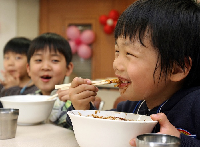 Black sauce noodles are one of the country's favorite delivery items. A child smiles as he enjoys his meal.