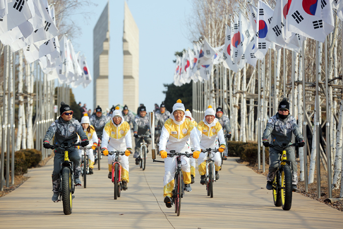 Torch bearers on bicycles pass by the <i>Baengma-goji</i> (백마고지), where the Battle of White Horse took place during the Korean War, in Cheorwon-gun County, Gangwon-do Province, on Jan. 21.