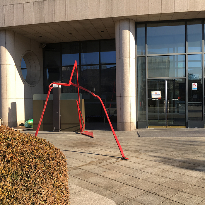 The red spider sculpture is located next to the smoking area and a trash can.