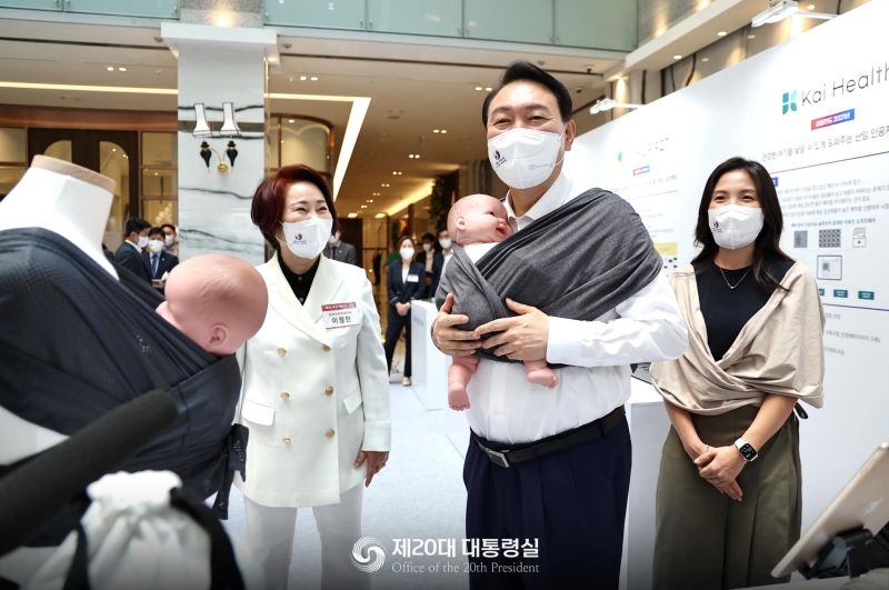 President Yoon Suk Yeol on July 5 visits the booth of Konny, a maker of baby care products, in the inaugural Women Entrepreneurs' Week and tries on a baby carrier at KBIZ Hall of the Korea Federation of SMEs in the Yeouido area of Seoul's Yeongdeungpo-gu District..
