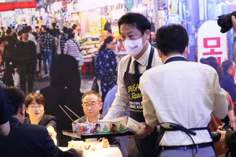 Cho Jae Il, director of the Korean Cultural Center (KCC) in Thailand, on the morning of May 2 at the KCC in downtown Bangkok serves food to visitors at the opening ceremony of an exhibition to promote Busan's bid to host the 2030 World Expo through the city's tourism and cuisine as shown in films. 
