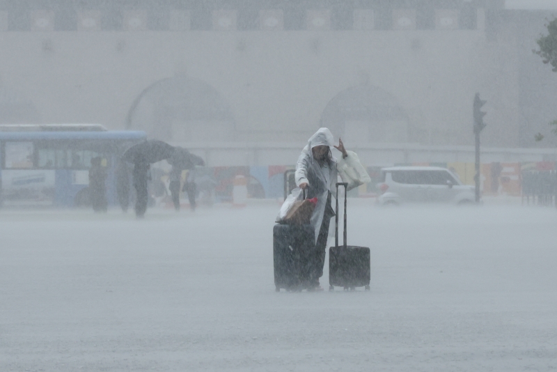 A raincoat-clad foreign tourist on the morning of June 29, the start of the summer monsoon season, walks through Gwanghwamun Square in Seoul's Jongno-gu District with a suitcase in tow.