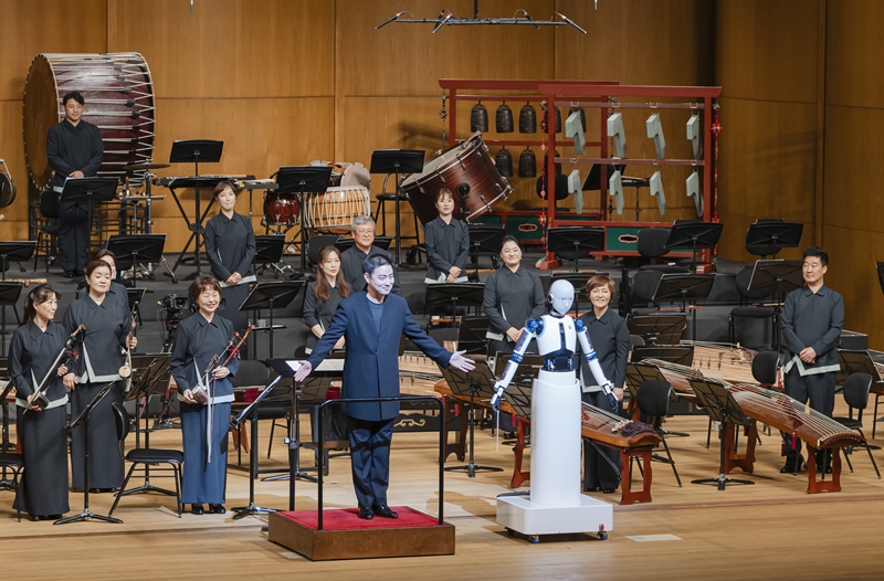 Conductor Soo-Yeoul Choi on June 30 imitates the arm pose of robot counterpart EveR 6 before both bow to the audience after performing 