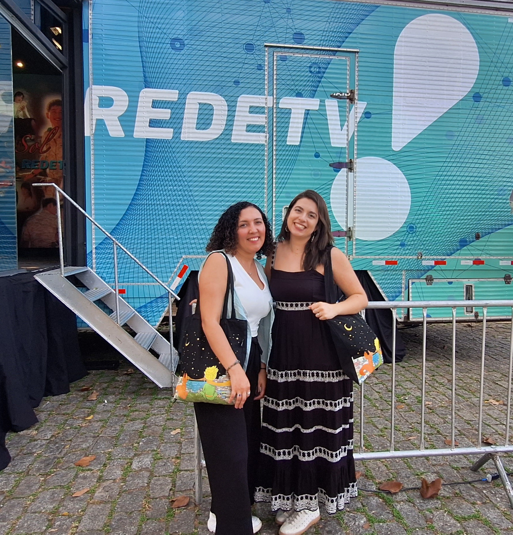 The two podcast hosts take a photo in front of a transmission bus of Rede TV.