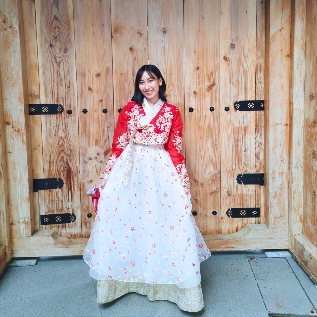 This photo of the writer has her wearing a red and white Hanbok with intricate designs.