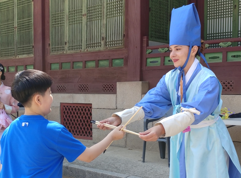 Festival volunteer Sarah Shalaby from France on May 1 explains how to play a traditional game to a child at Gyeongchunjeon Hall of Changgyeonggung Palace at the spring edition of this year's K-Royal Culture Festival. 