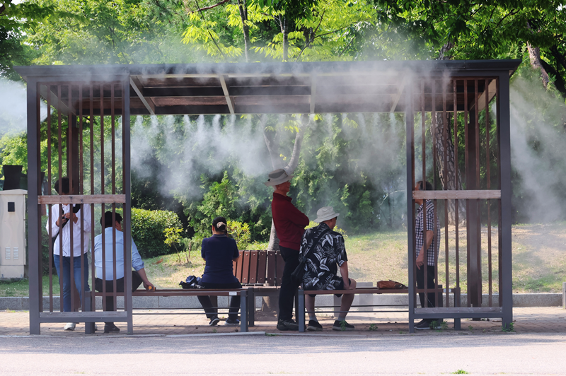 People in June stand under a sprinkler spraying cooling fog at Yeouido Park in Seoul's Yeongdeungpo-gu District. (Yonhap News) 