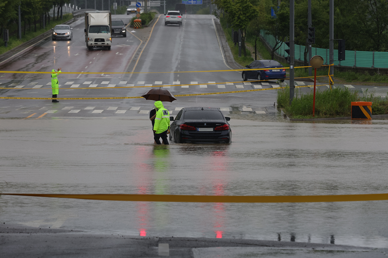 Drivers from this month can get flood alerts on the road through map apps or navigation systems. Shown is a police officer on the morning of July 18 escorting the driver of a car stuck in a flood to a safe place near Munsan Station in Paju, Gyeonggi-do Province. (Yonhap News) 