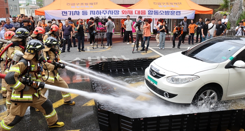 As part of a joint drill to put out a fire in an electric vehicle, firefighters on Aug. 27 spray a towed car using a mobile water tank at the underground parking lot of Yeonji Raemian Urban Park in Busan's Busanjin-gu District. 