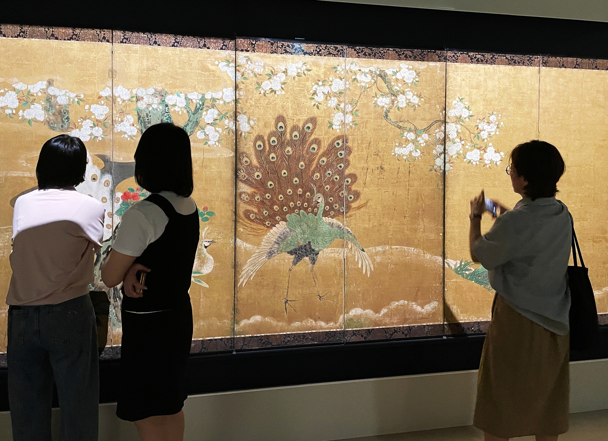 Visitors on June 16 look at a folding screen decorated with a phoenix and a peacock at a media event marking the opening of the exhibition 