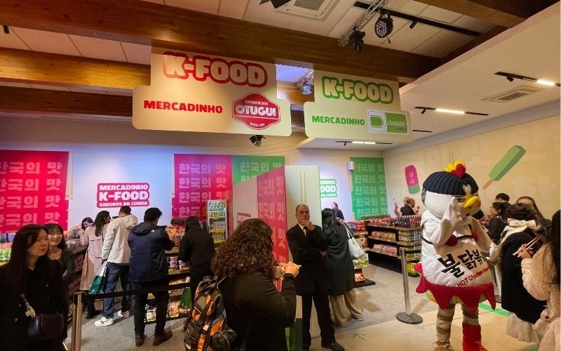 Visitors enjoying the Universe K-Food Brazil event, with the convenience and pop-up stores visible in the background.
