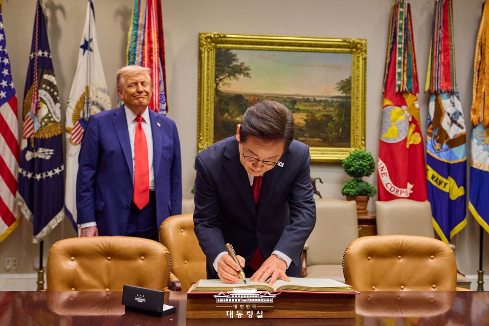 President Lee Jae Myung on Aug. 25 signs the guestbook of the Oval Office at the White House in Washington with U.S. President Donald Trump looking on. (Office of the President)