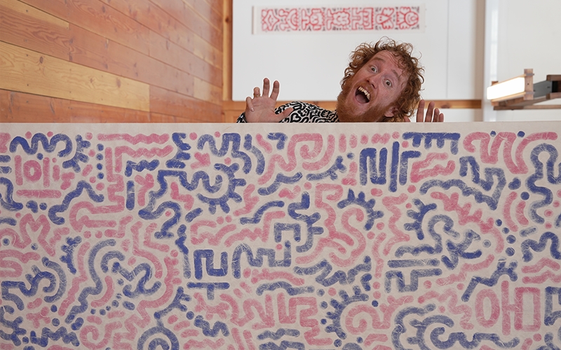 Cox, playfully poses alongside his intricate doodle work on hanji, the traditional handmade mulberry paper. [Image Courtesy: Sam Cox]