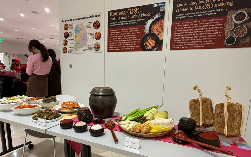 An exhibition table features realistic food models, including different kimchi varietes and rice, representing traditional Korean dishes.