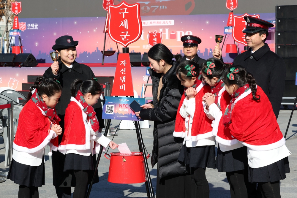 Children on Nov. 28 slip an envelope with a donation into a charity kettle on Myeong-dong Street in Seoul's Jung-gu District.