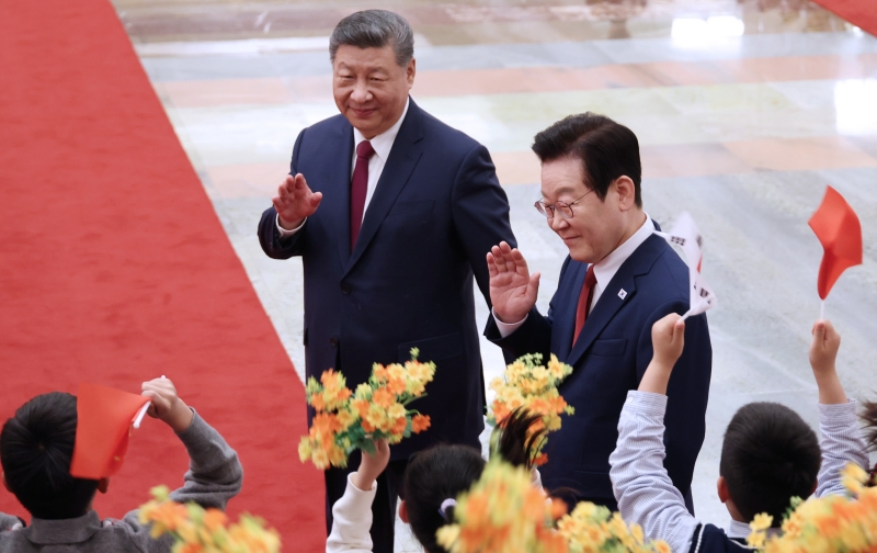 President Lee Jae Myung (right) and Chinese President Xi Jinping on Jan. 5 wave at children attending the official welcoming ceremony for both leaders at the Great Hall of the People in Beijing. (Yonhap News)