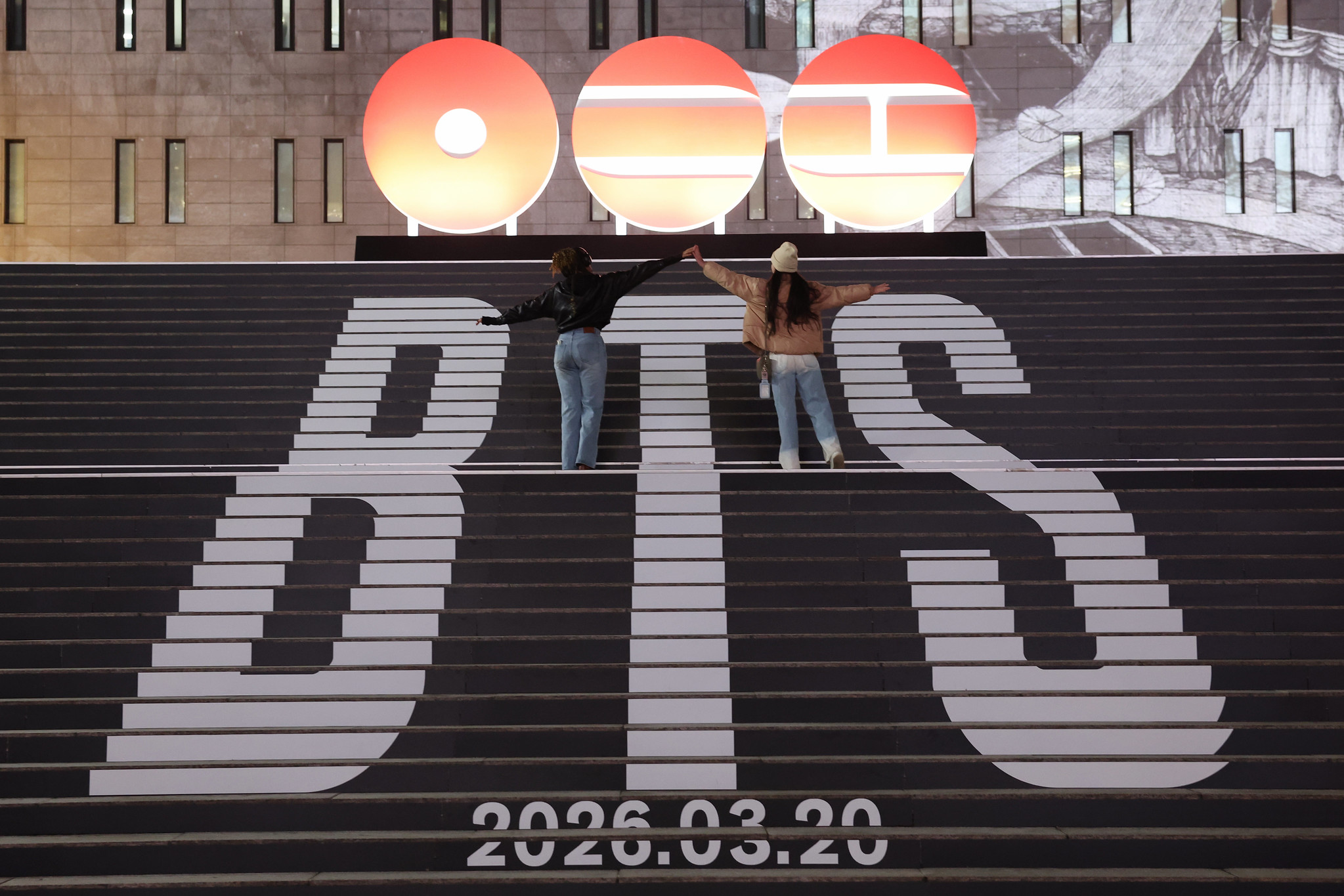 Two BTS fans on the central staircase leading up to Sejong Center for the Performing Arts in Seoul's Jongno-gu District on Jan. 6 pose for photos ahead of the K-pop phenom's highly anticipated return in March. (Lee Jeongwoo)  