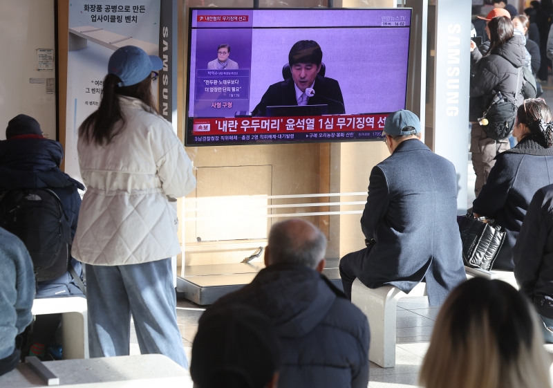 People at Seoul Station on Feb. 19 watch live presiding Judge Ji Gwi-yeon of the Seoul Central District Court in the first trial of former President Yoon Suk Yeol on the charge of masterminding the failed martial law attempt on Dec. 3, 2024. (Yonhap News)  