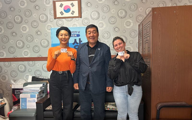 Kylie Genter (right) poses for a photo with Kim Chang-shik, the fishery chief of Yeongrak-ri (center) and fellow diver Choi Jung-yoon holding their haenyeo licences at the Yeongrak-ri Fishery Office in Jeju Island in April 2026.