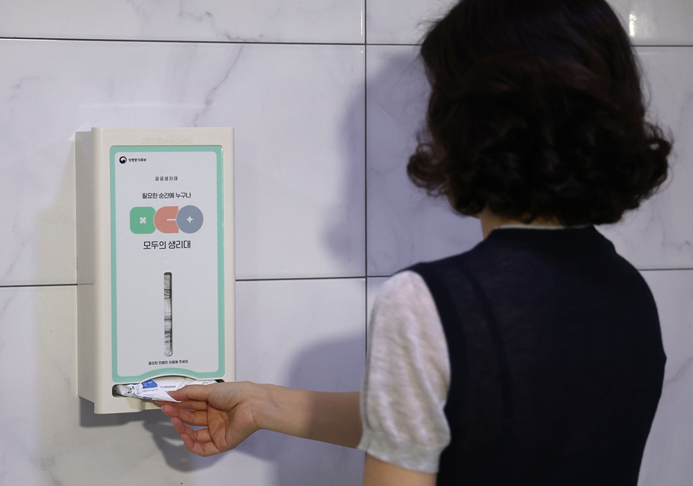 A woman on July 6 pulls out a sanitary pad from a public dispenser at a restroom of Eunpyeong Women's Development Center in Seoul's Eunpyeong-gu District on the first day of a pilot program for providing free pads. (Yonhap News)