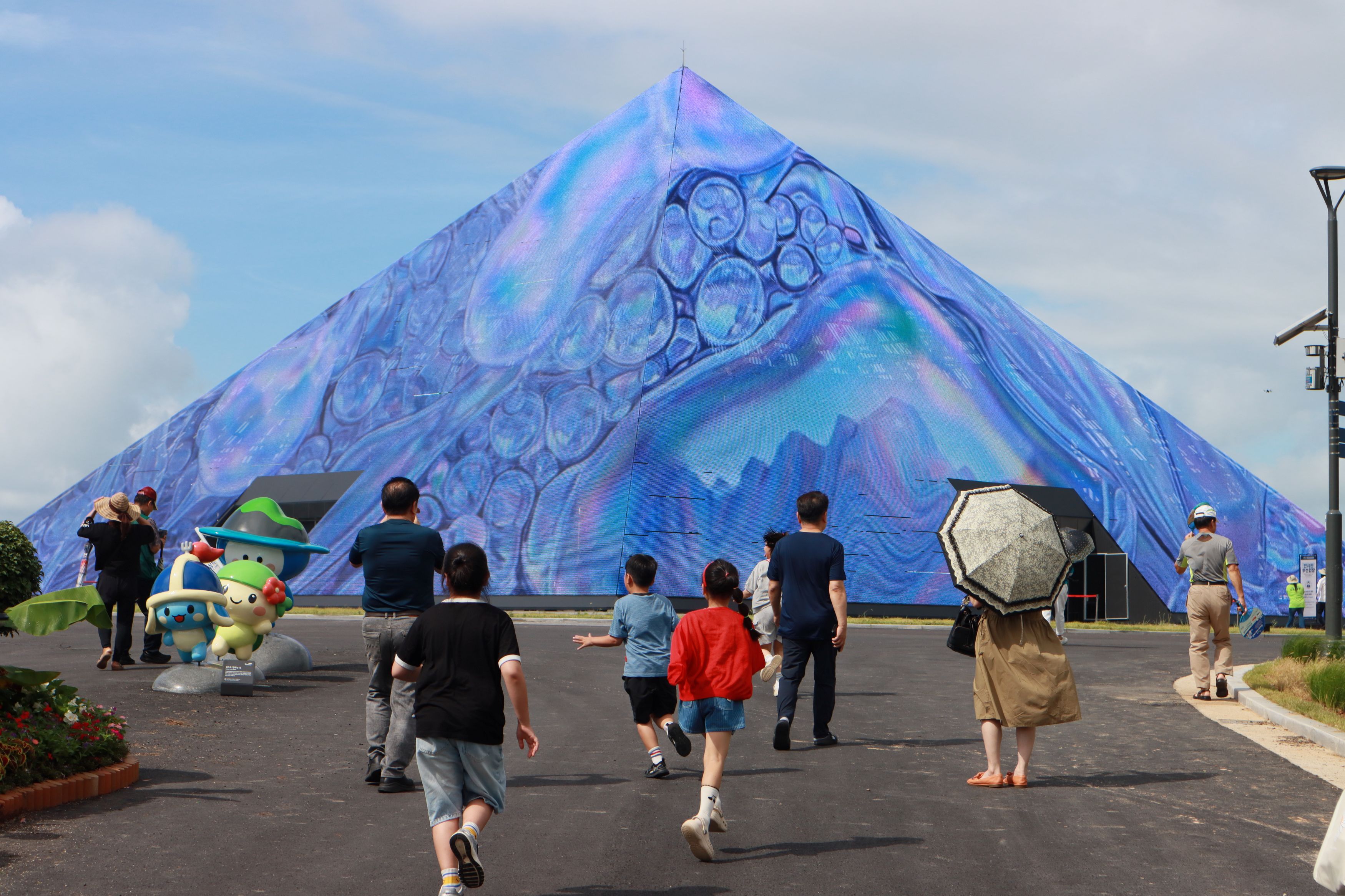Visitors on Aug. 29, about a week before the opening of the inaugural World Island Fair, walk in front of the media facade of the exhibition hall Theme Island on a preview day at the main venue of Dolsando Island off the coast of Yeosu, Jeollanam-do Province. (Event's organizing committee) 