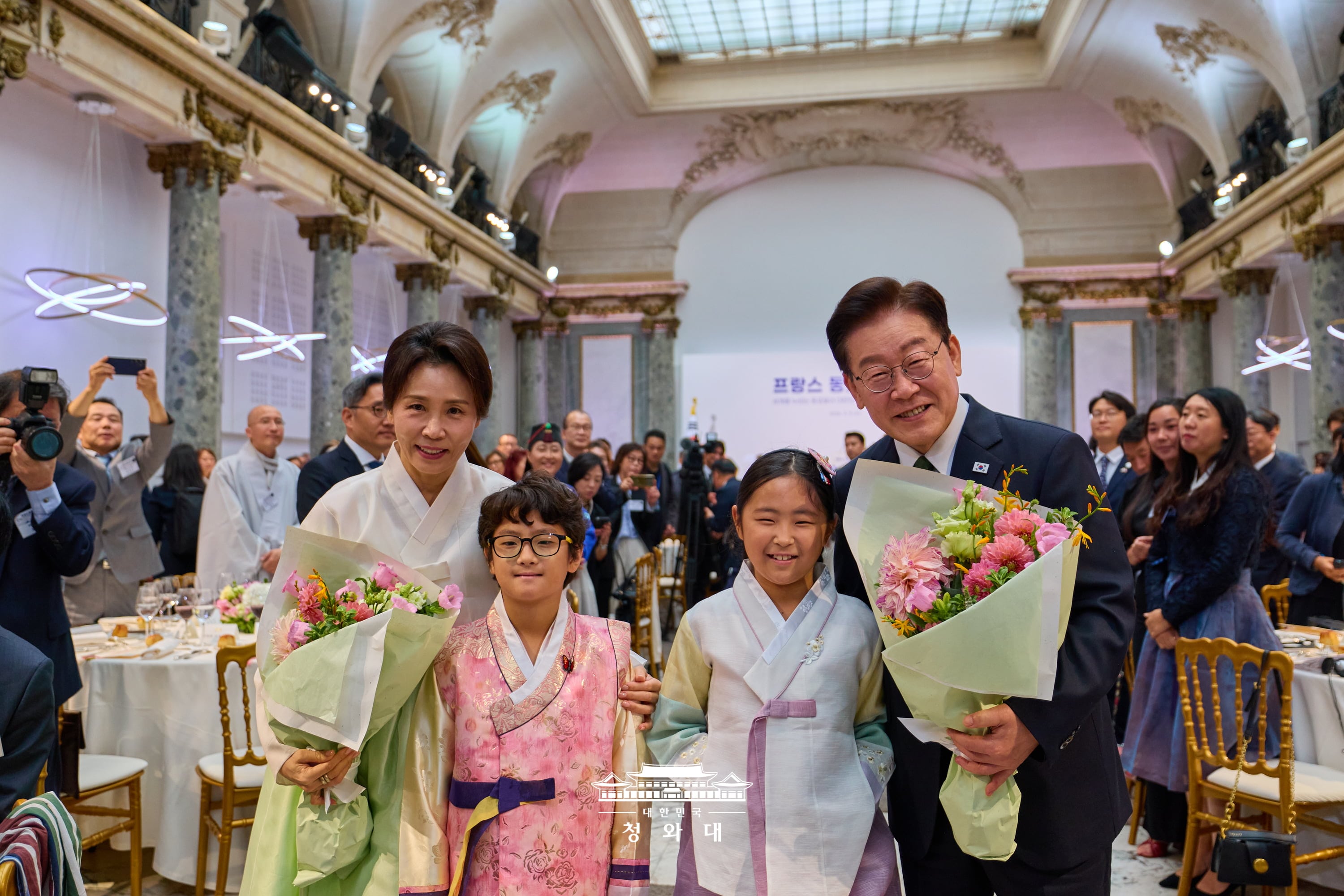 President Lee Jae Myung (right) and first lady Kim Hea Kyung on Sept. 9 hold bouquets presented by children at a luncheon with ethnic Koreans in France at the historic event venue Pavillon Cambon Capucines in Paris. 