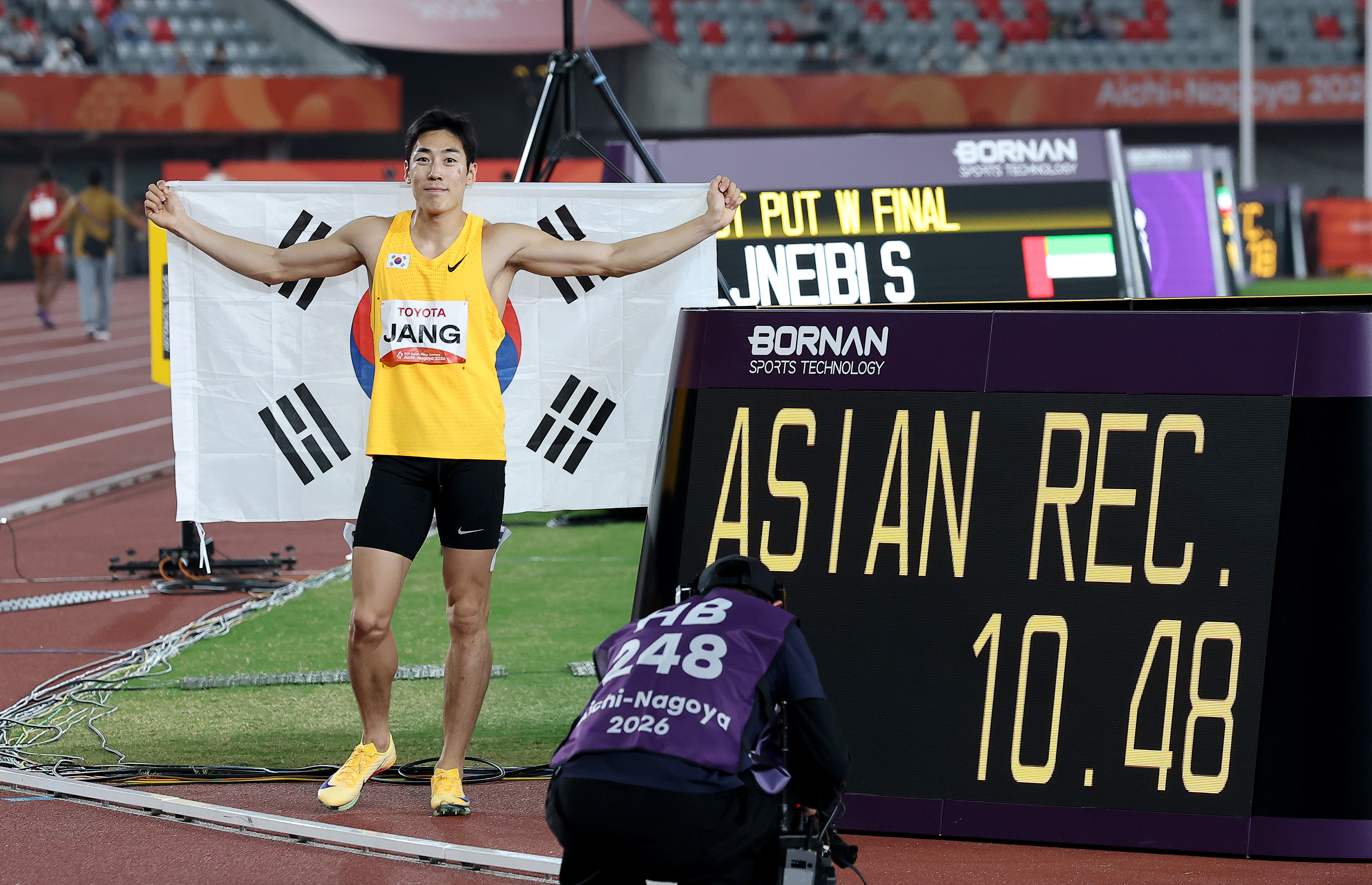 Sprinter Jang Minho on Oct. 20 poses for a photo next to a scoreboard showing his Asian record time of 10.48 seconds after winning the men's 100 m (T13) at the Aichi-Nagoya Asian Para Games at Paloma Mizuho Stadium in Nagoya, Japan.