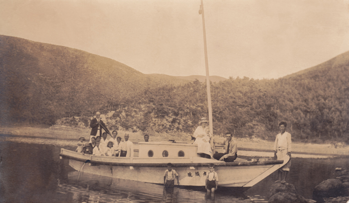 Rev. James Nobel Mackenzie (far left) holds a paddle on a yacht. (photo courtesy of the KCC, Australia)